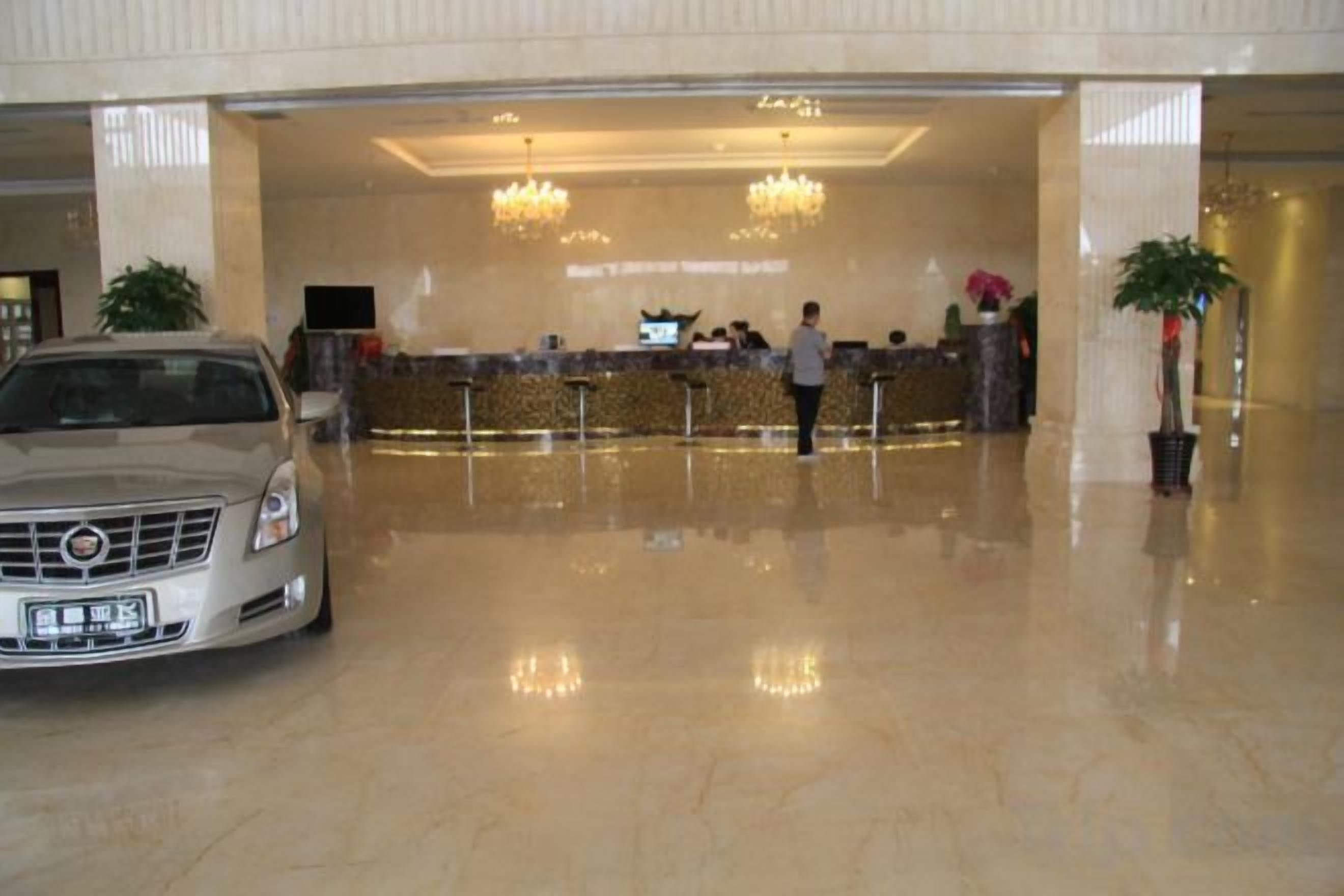 Een hotel receptie met een auto ervoor, een receptiebalie en een grote kroonluchter.