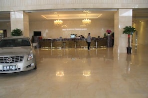 Un hall d'hôtel avec une voiture garée devant, un comptoir d'accueil et un grand lustre.