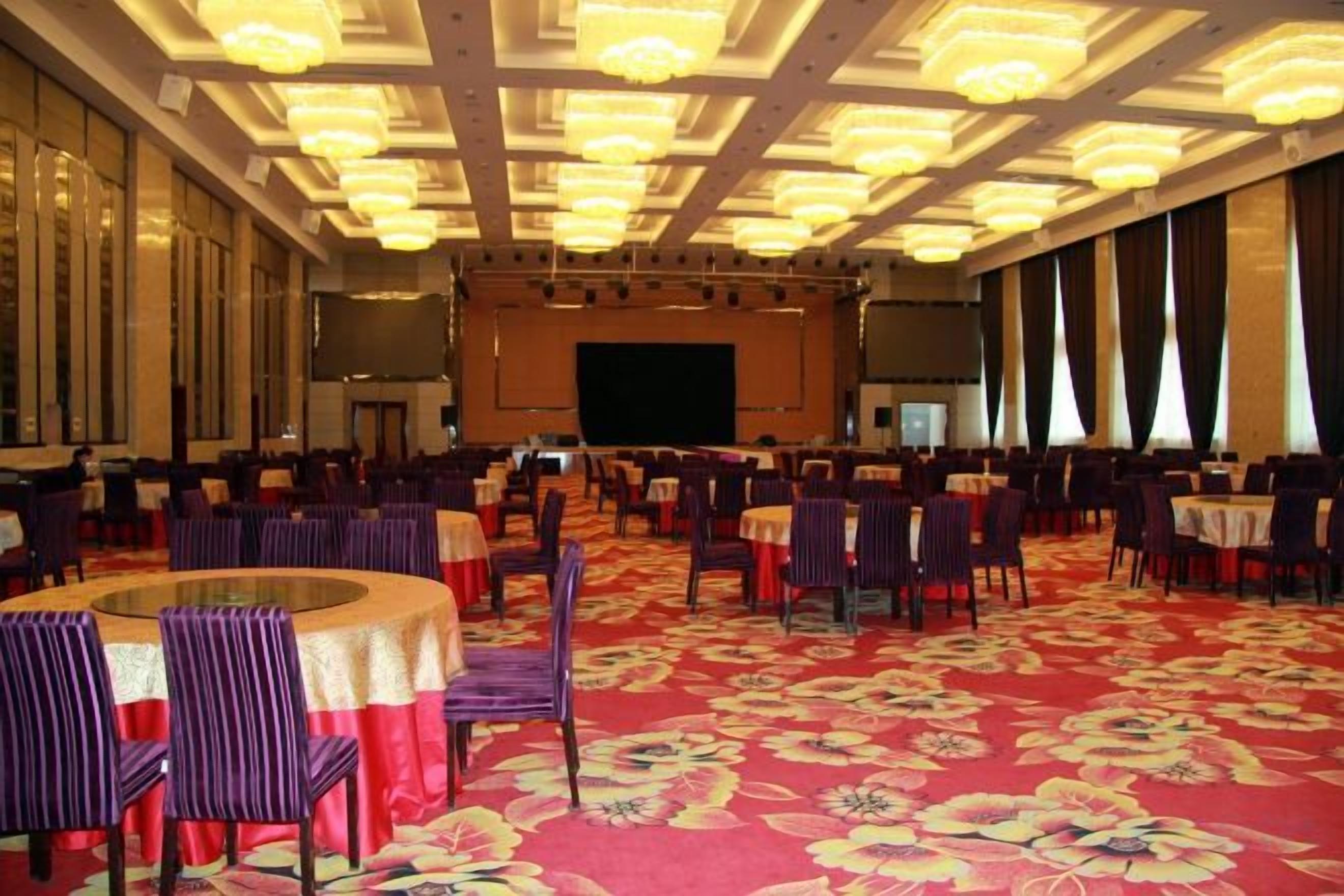 A banquet hall with round tables and chairs, a stage, and a large screen.