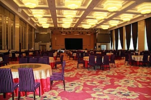 Un salón de banquetes con mesas y sillas redondas, un escenario y una pantalla grande.