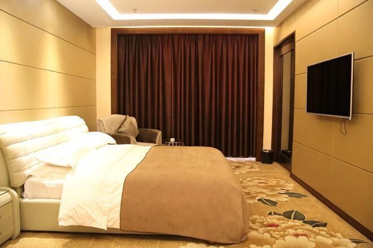 Een hotelkamer met een bed, een stoel, een televisie en een groot raam met gordijnen.