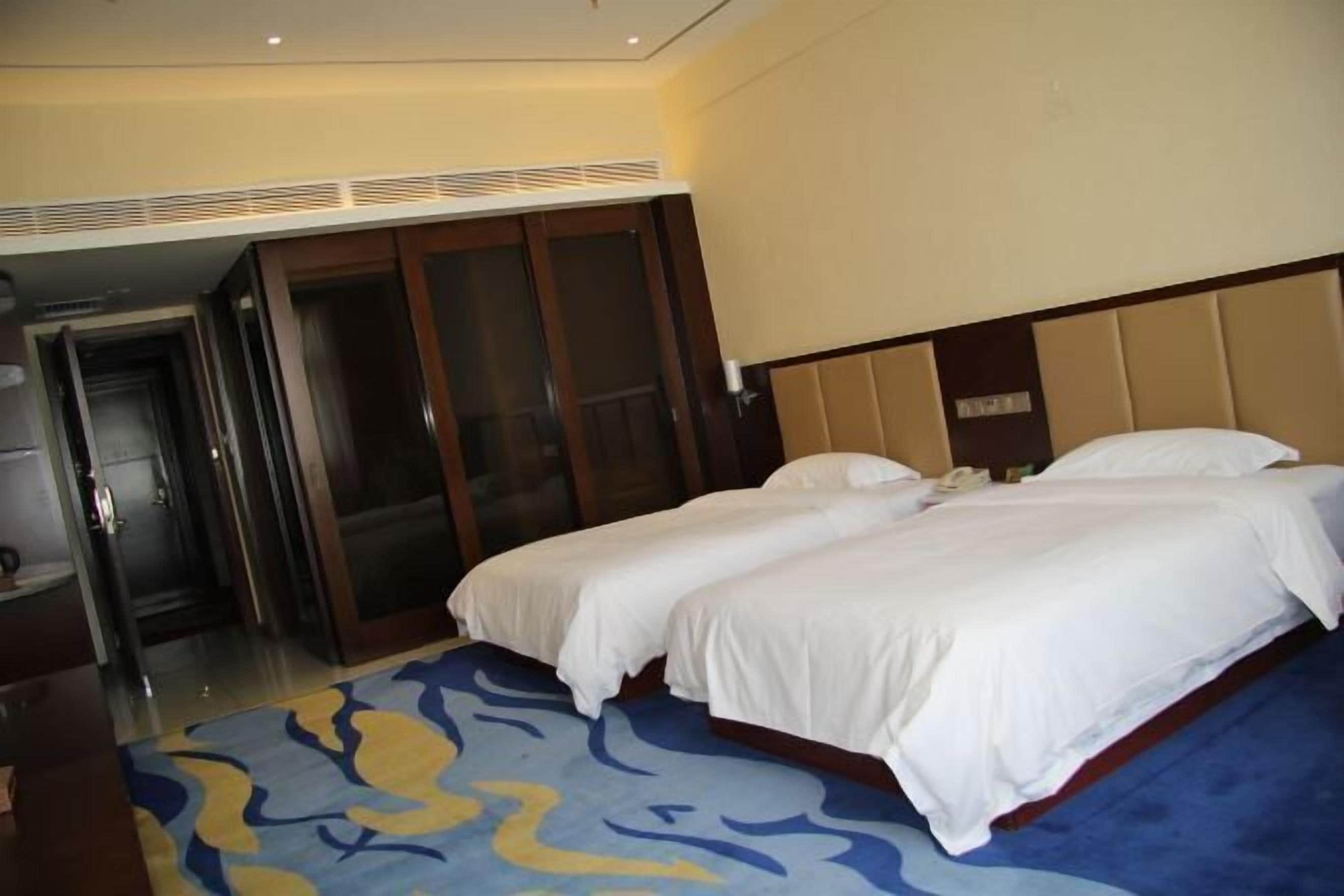 Habitación de hotel con dos camas, un espejo grande y una puerta que da a un pasillo.