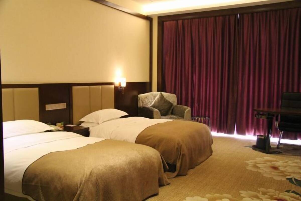 Een hotelkamer met twee bedden, een stoel, een bureau en een groot raam met gordijnen.