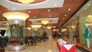 A spacious lobby with a central glass display, multiple seating areas, and a long table set for dining.