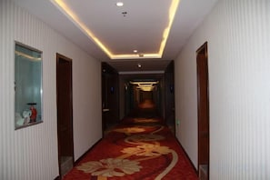 A hotel hallway with a patterned carpet, doors on both sides, and a ceiling with recessed lighting.