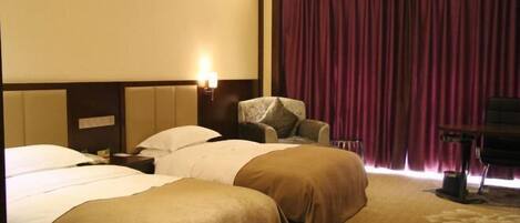 A hotel room with two beds, a chair, a desk, and a large window with curtains.