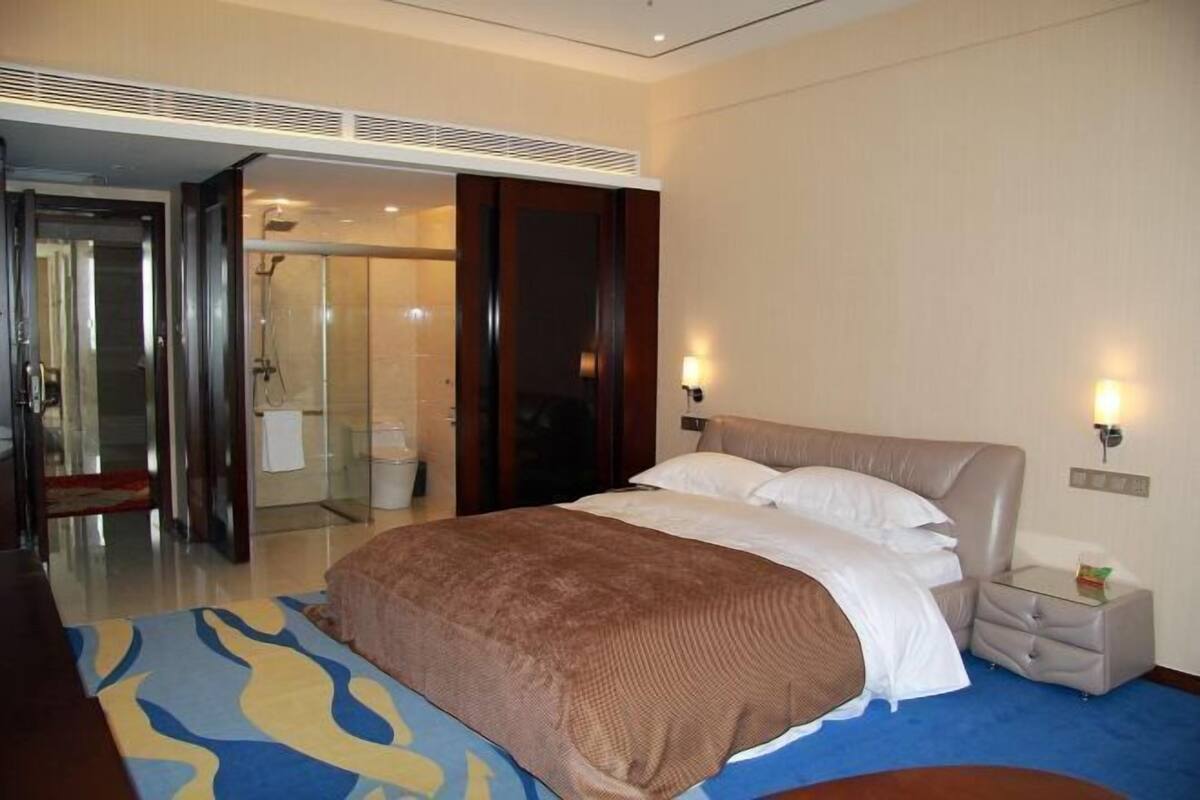 Een hotelkamer met een bed, nachtkastjes, een badkamer en een glazen deur naar een douchecabine.