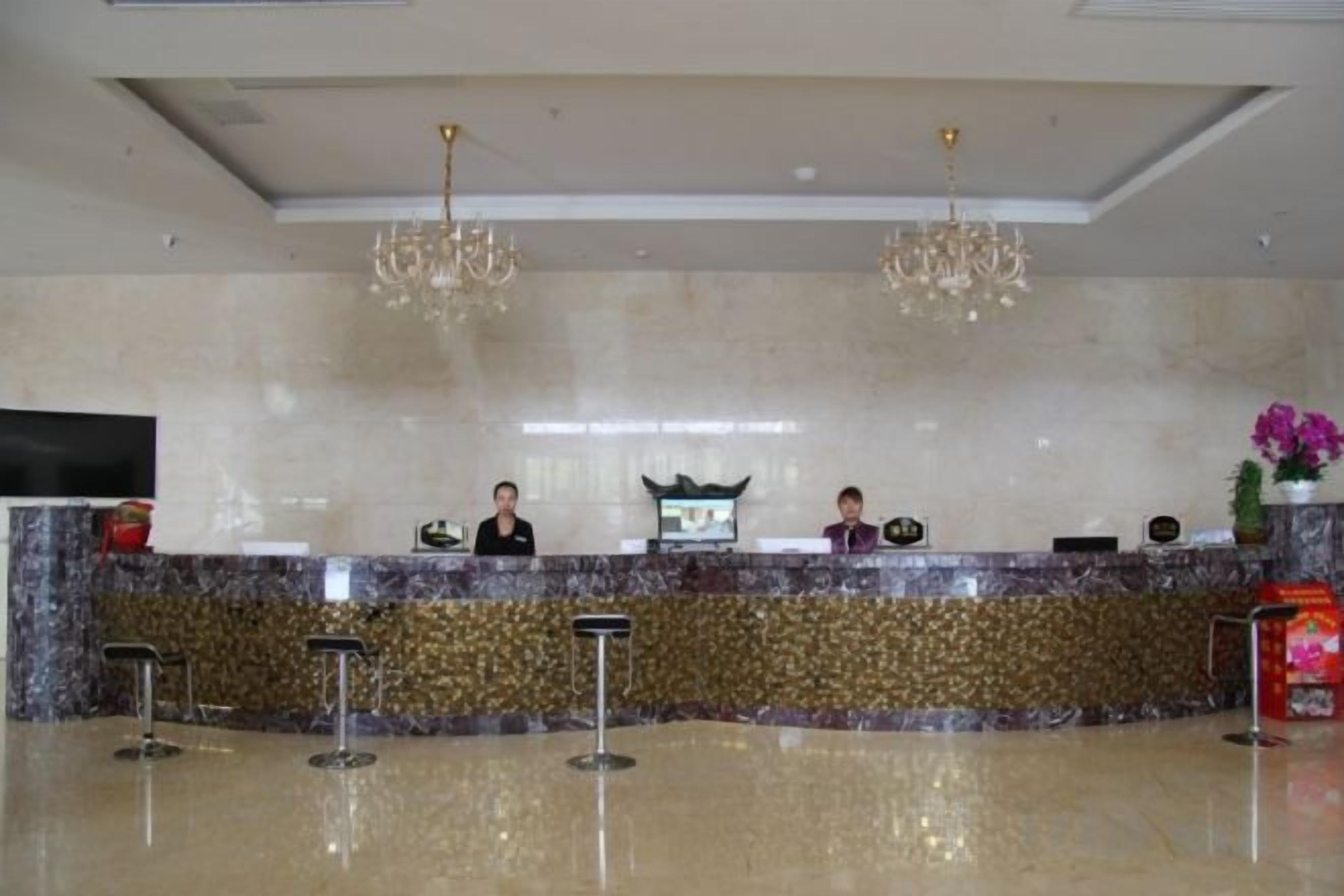 A hotel reception area with a marble counter, two receptionists, and a television screen.