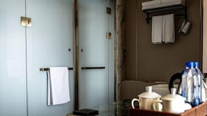 A hotel room with a glass partition, a wooden counter with a tray of toiletries, and a towel rack with two towels.