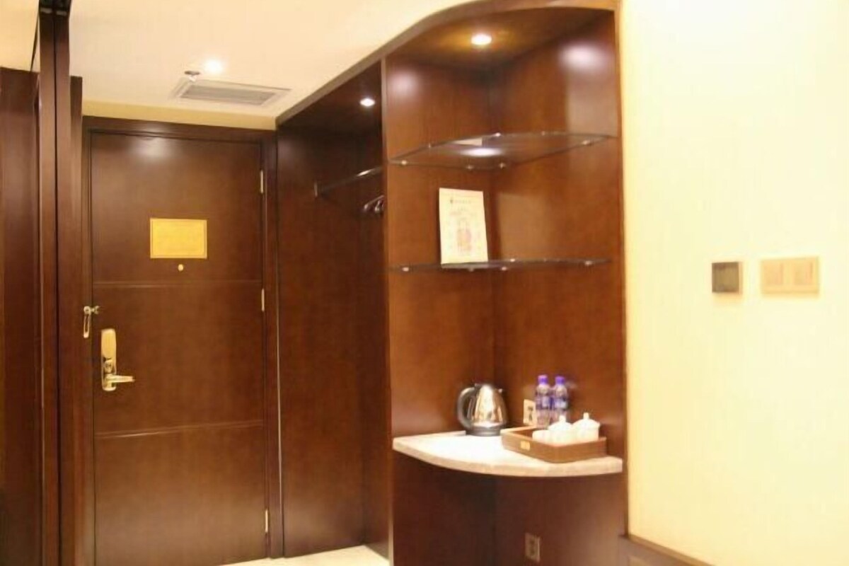 Une chambre d’hôtel avec une porte en bois, un petit bureau avec une bouilloire et une étagère avec des bouteilles d’eau.