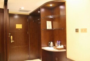 Une chambre d’hôtel avec une porte en bois, un petit bureau avec une bouilloire et une étagère avec des bouteilles d’eau.
