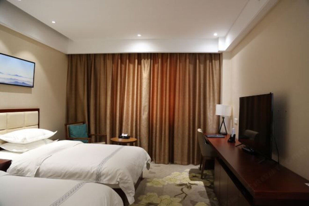 Habitación de hotel con dos camas, un escritorio, televisión y un amplio ventanal con cortinas.