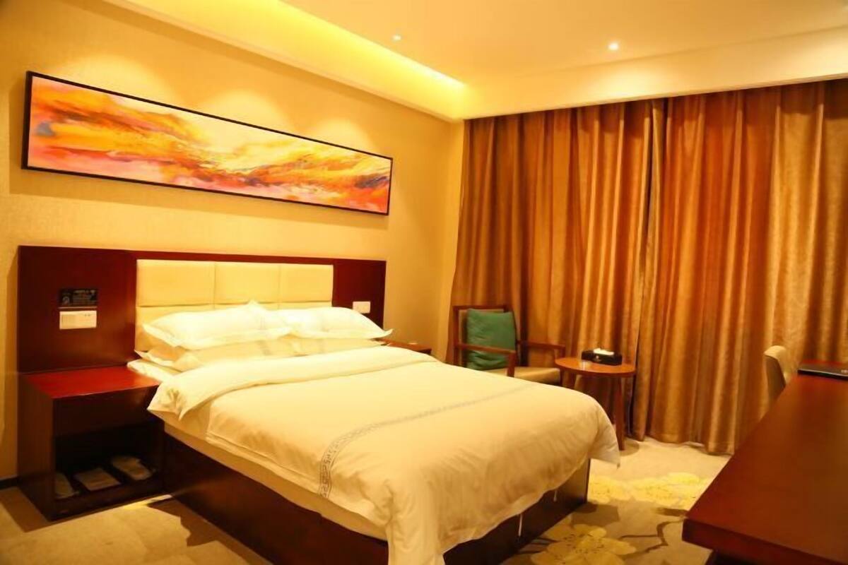 Une chambre d’hôtel avec un grand lit, un bureau, une chaise, une télévision et un tableau au mur.