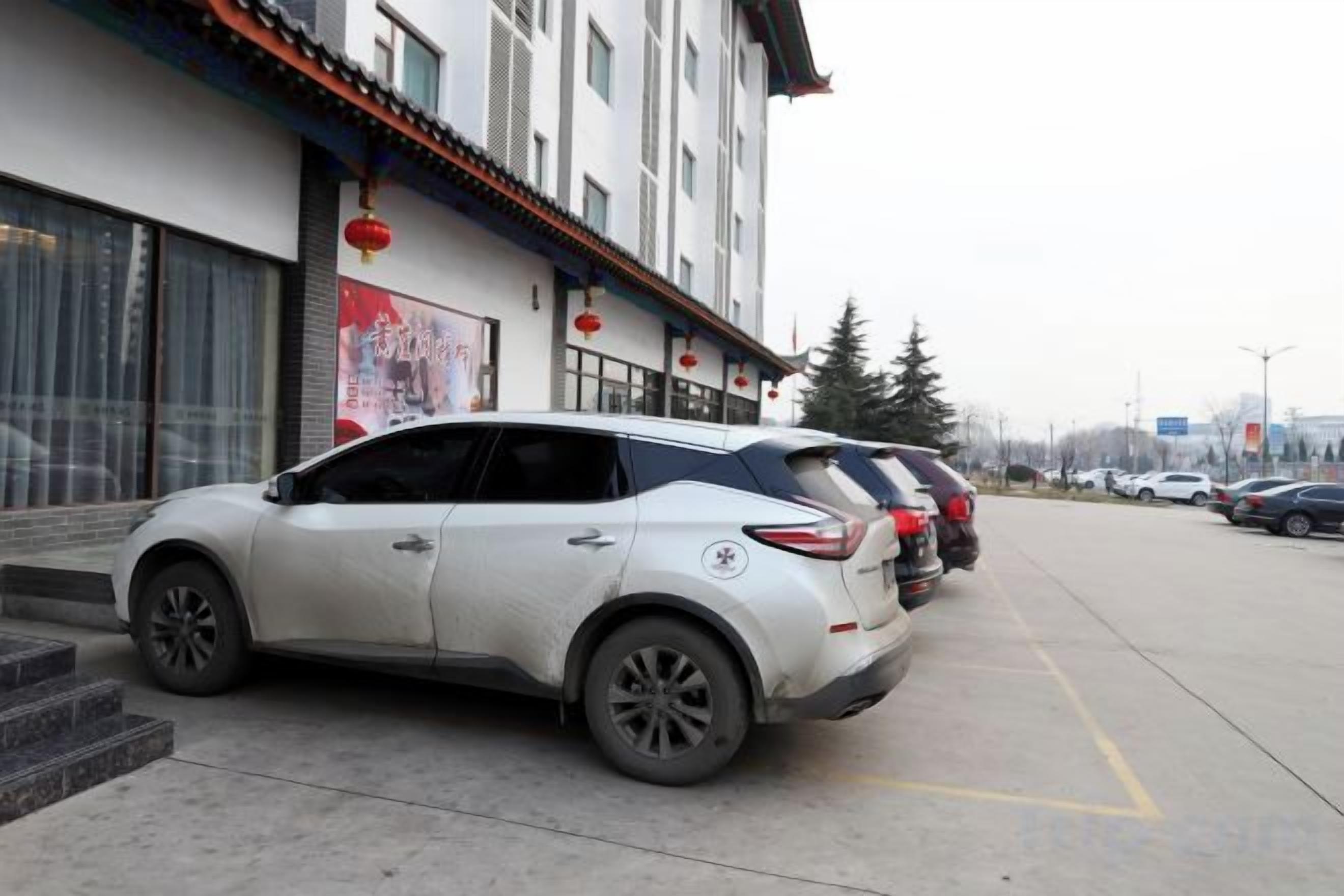A white SUV parked in front of a building with a traditional architectural style, including a tiled roof and red lanterns.