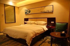 Une chambre d’hôtel avec un grand lit, une table de chevet avec une lampe, une petite table ronde avec un verre, et un tableau accroché au mur.