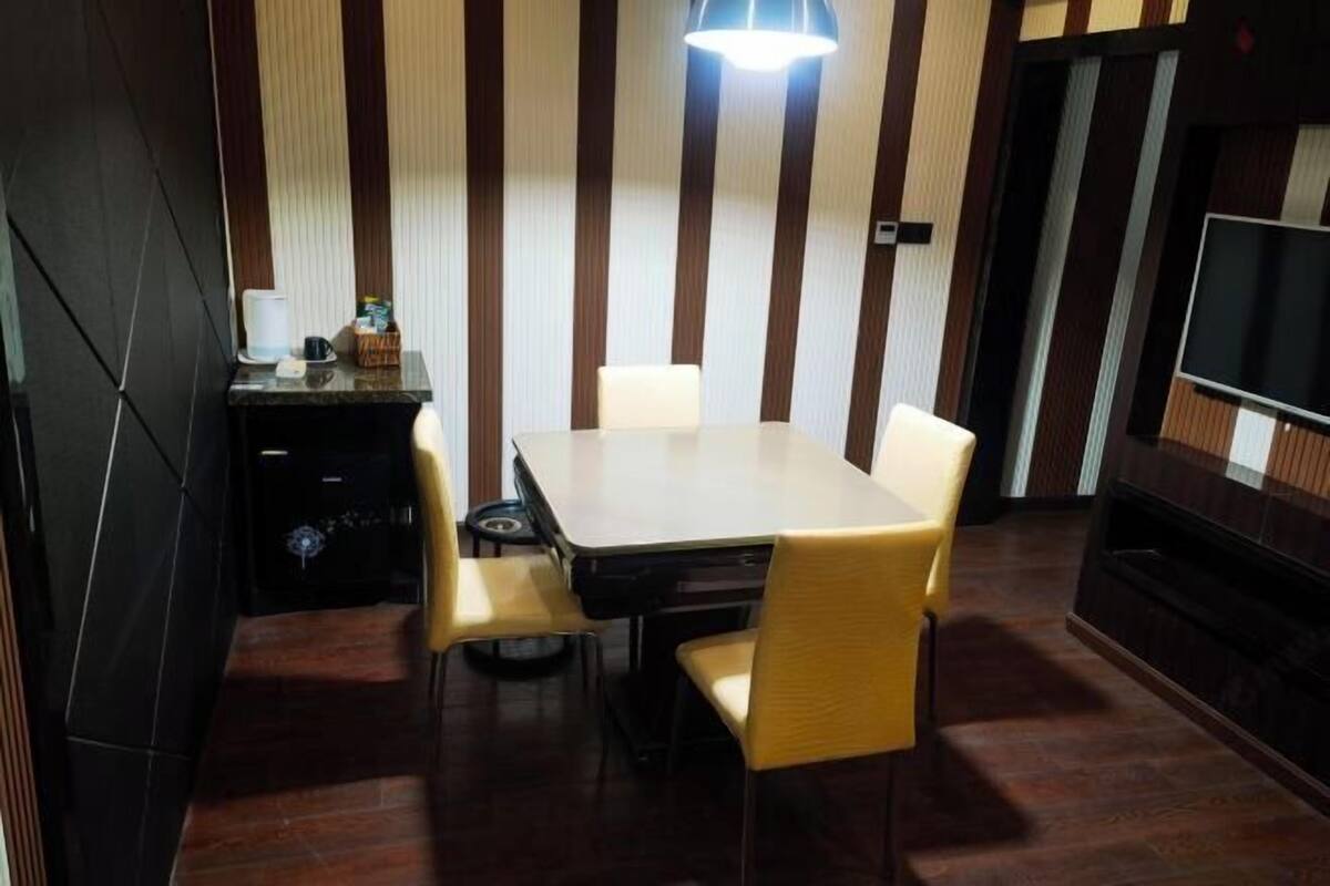 Uma área de refeições com uma mesa retangular e quatro cadeiras, uma máquina de café e uma televisão à direita.