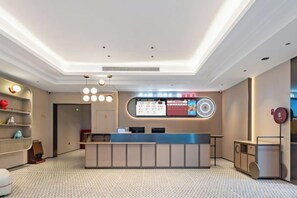 A hotel reception area with a reception desk, a digital display board, and a patterned carpet. - Shangkeyou Nantong Haimen Pedestrian Street Hotel (Nantong)