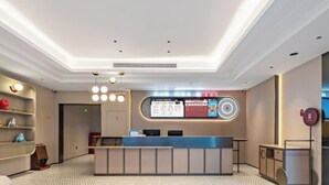 Un moderno hall de hotel con mostrador de recepción, pantalla informativa digital y una alfombra estampada.