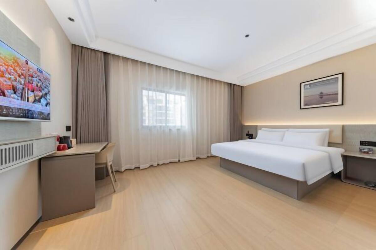 Quarto de hotel moderno com cama, escrivaninha, cadeira, televisão e janela com cortinas.