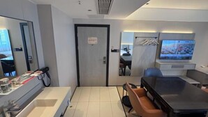 Una habitación de hotel moderna con una cama grande, un escritorio, una silla, un televisor y un baño con espejo y lavabo.