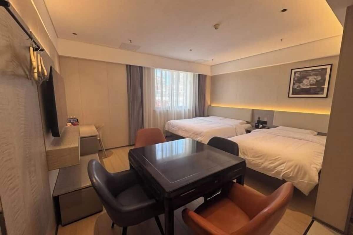 Quarto de hotel com cama, secretária com cadeiras, televisão e janela com cortinas.