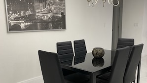 Zona pranzo con tavolo in vetro, sedie nere, lampadario e dipinto di un panorama urbano sulla parete.