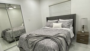Una camera da letto con un letto, un comodino, una lampada, una ventola a soffitto e una finestra con persiane.