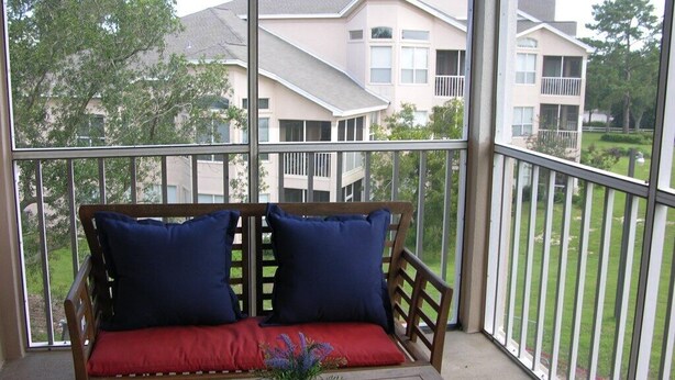 Een balkon met een houten bankje en een tafel, met uitzicht op een woongebied met huizen en groen.