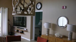 Een eetruimte met een ronde tafel en rode stoelen, een houten kast met decoratieve lampen, en een aan de muur bevestigde televisie.