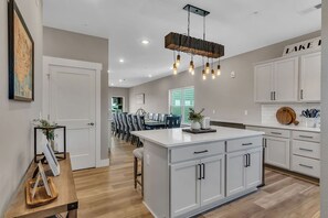 Uma cozinha moderna com armários brancos, uma ilha central e um lustre.