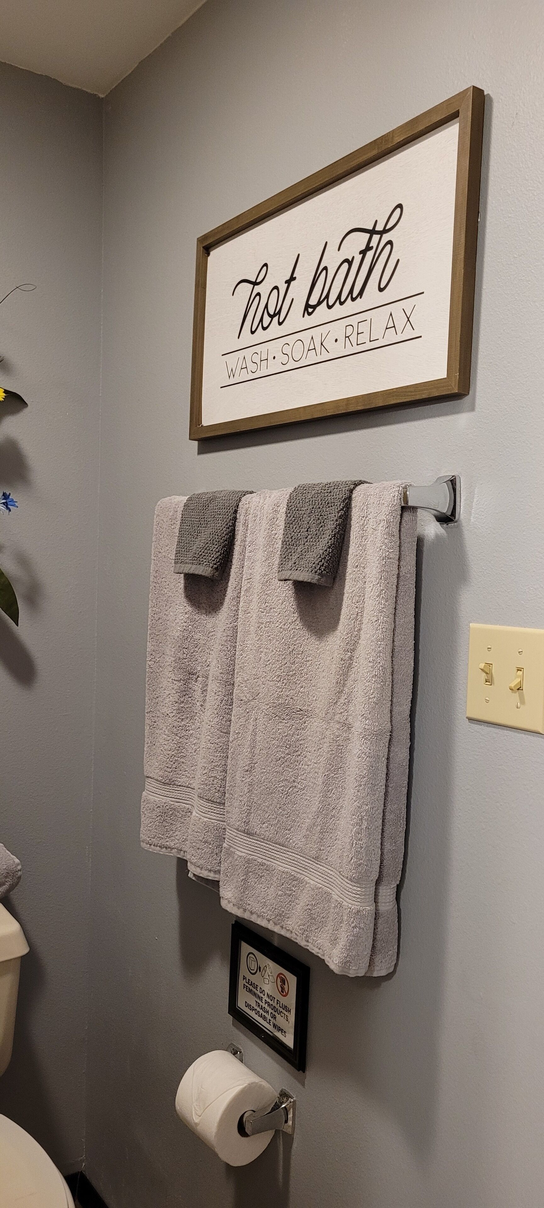 A bathroom with a framed sign that reads "Hot bath WASH. SOAK. RELAX" and two towels hanging on a rack.