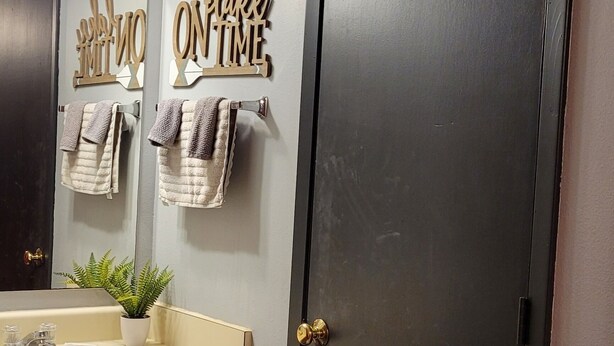 A bathroom with a wooden vanity, a sink, a mirror, a towel rack with towels, and a dark door. - Fun In The Sun #11 (Karnack)
