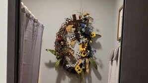 A bathroom with a toilet, a towel rack, a shower curtain, and a decorative wreath on the wall. - Fun In The Sun #11 (Karnack)