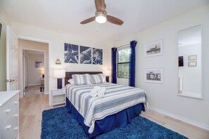 A bedroom with a bed, a ceiling fan, a window with curtains, and wall art.