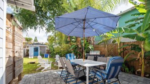 A patio with a table and chairs, a grill, and a blue umbrella. - 1/2 Mile to Beach, 2 bedroom townhome close to Mayo Clinic (Jacksonville Beach)