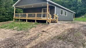 A single-story house with a covered porch and a wooden deck. - Hidden Hideway, fully furnished home perfect for family get aways! (Boyne City)