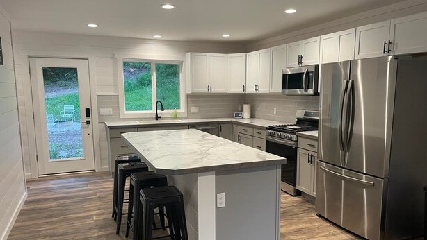 A modern kitchen with white cabinets, stainless steel appliances, and a marble island. - Hidden Hideway, fully furnished home perfect for family get aways! (Boyne City)