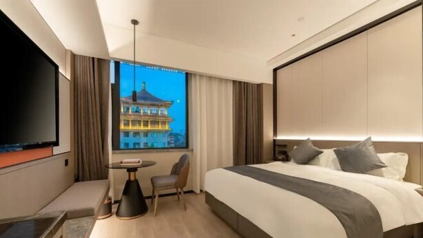Habitación de hotel moderna con una cama grande, televisi ón, una mesita y vistas a un edificio tradicional.