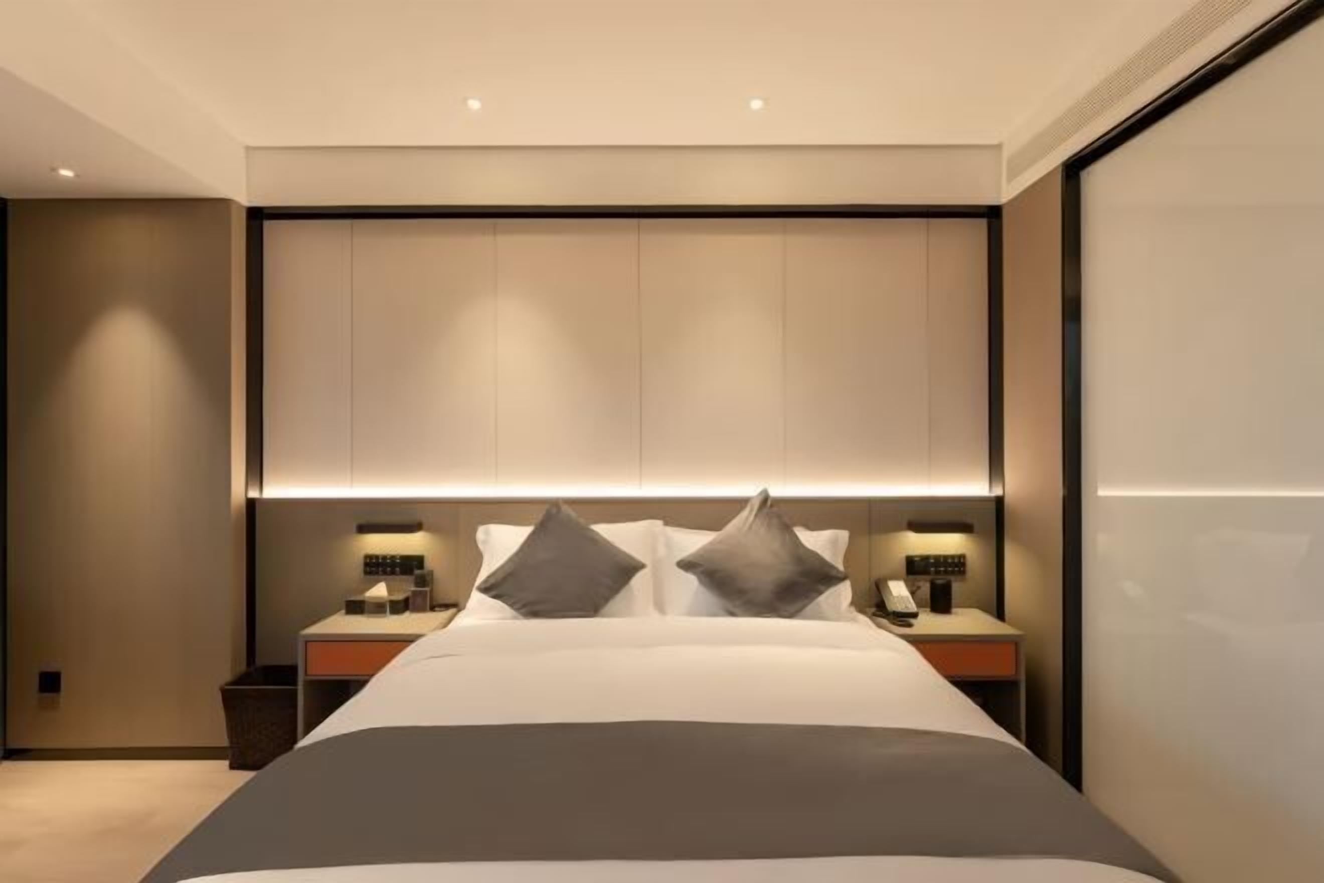 Una habitación de hotel moderna con una cama grande, mesitas de noche y un cabecero con iluminación integrada.
