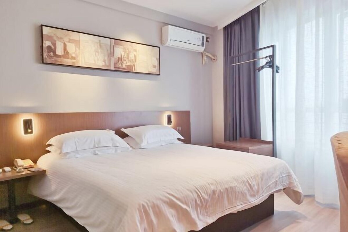 A hotel room with a large bed, a bedside table with a phone, and a window with curtains.