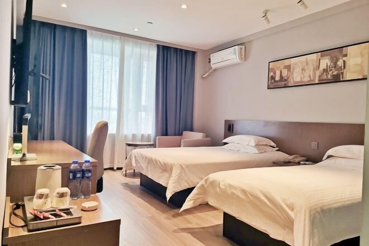 A hotel room with two beds, a desk with a chair, a TV, and a window with curtains.