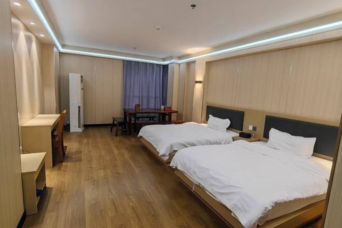 A hotel room with two beds, a desk, a chair, and a wardrobe.
