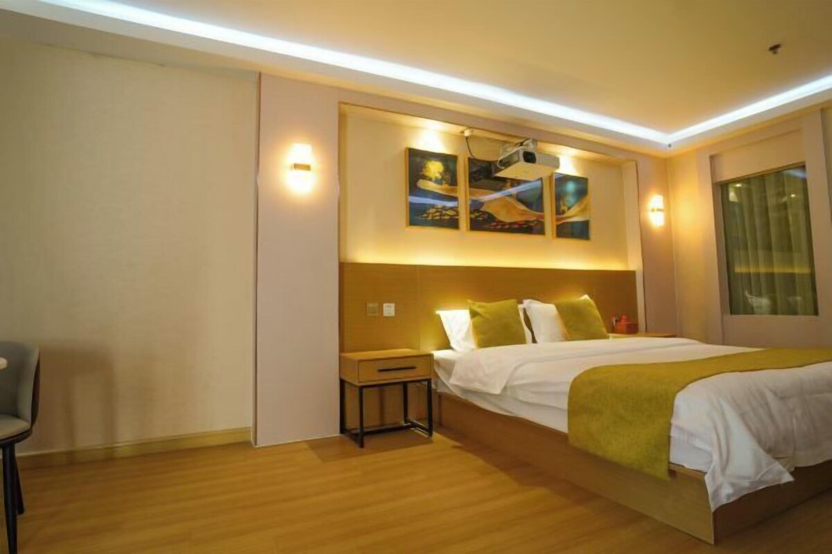 Una habitación de hotel con cama, mesita de noche, lámpara, obra de arte y ventana.