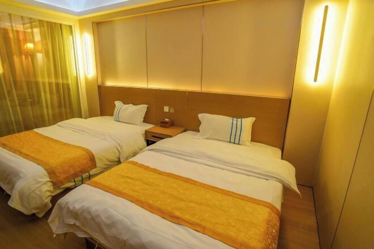 A hotel room with two beds, a nightstand, and a headboard with built-in lighting.