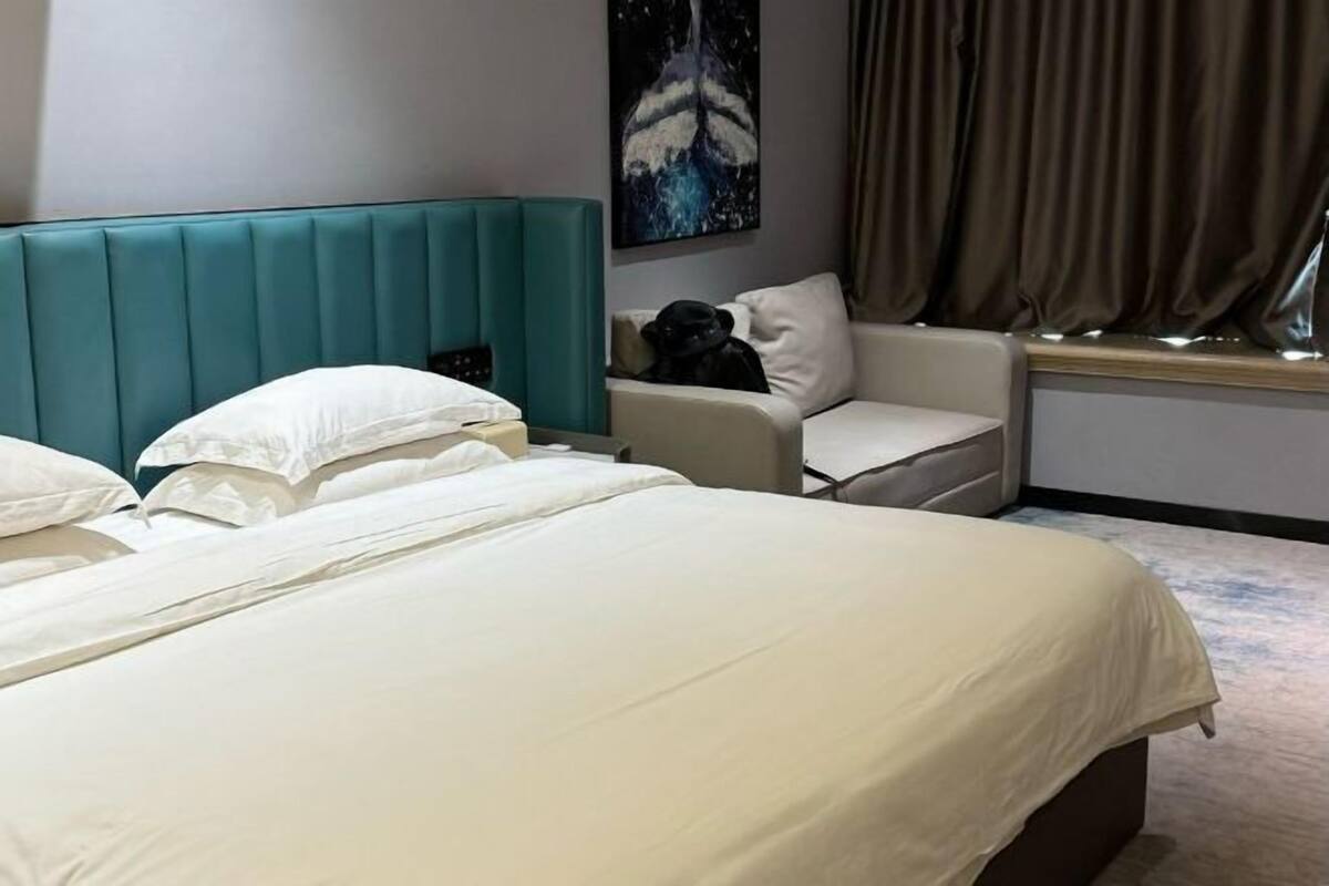 A hotel room with a large bed, a sofa, a window with curtains, and a painting on the wall.