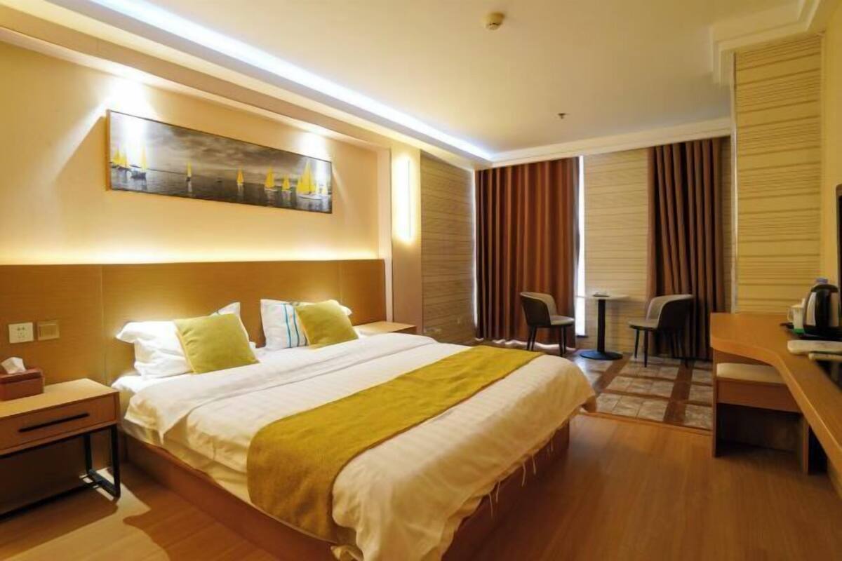 A hotel room with a bed, bedside table, lamp, and a painting on the wall.