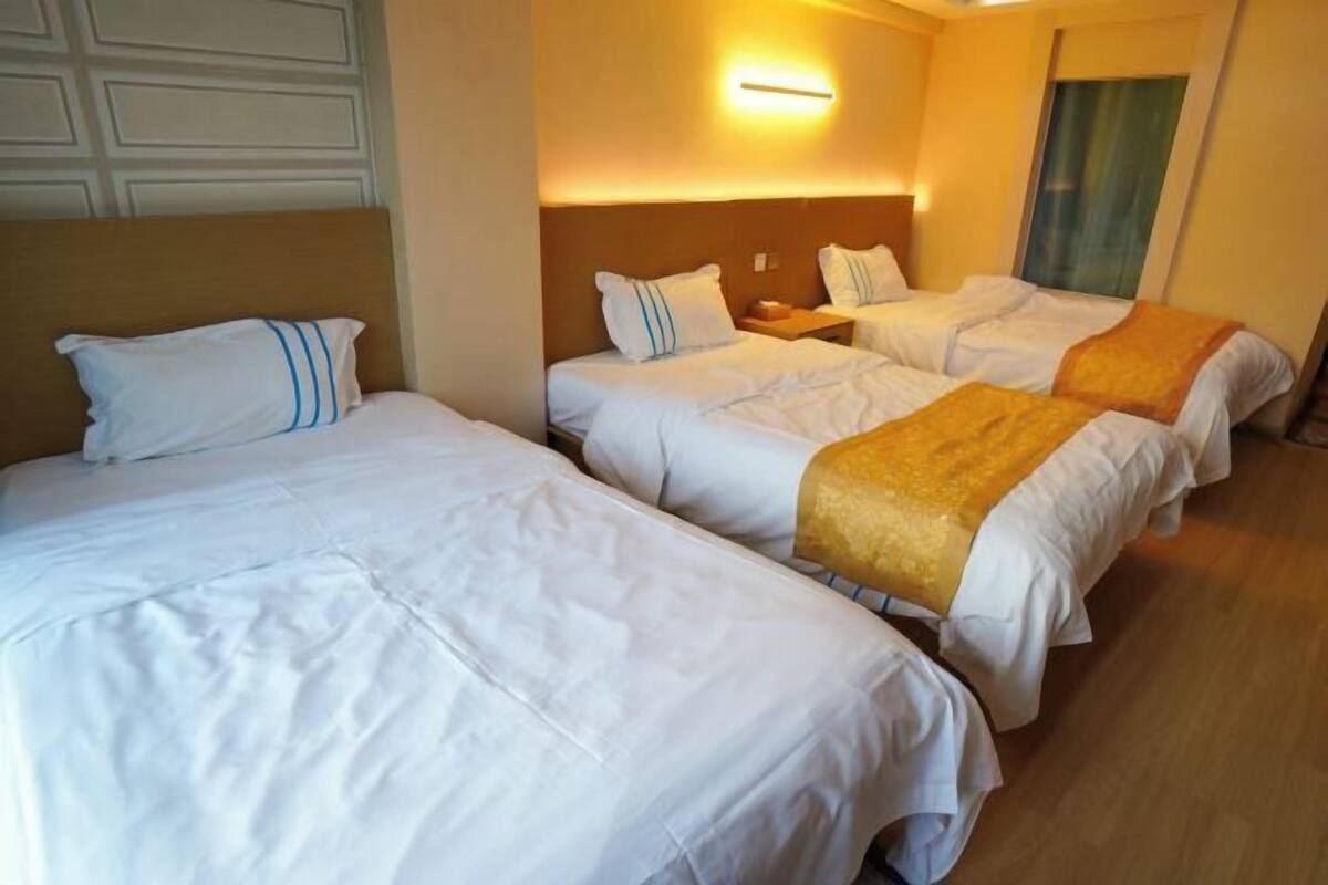 A hotel room with two beds, a nightstand, and a wall-mounted light.