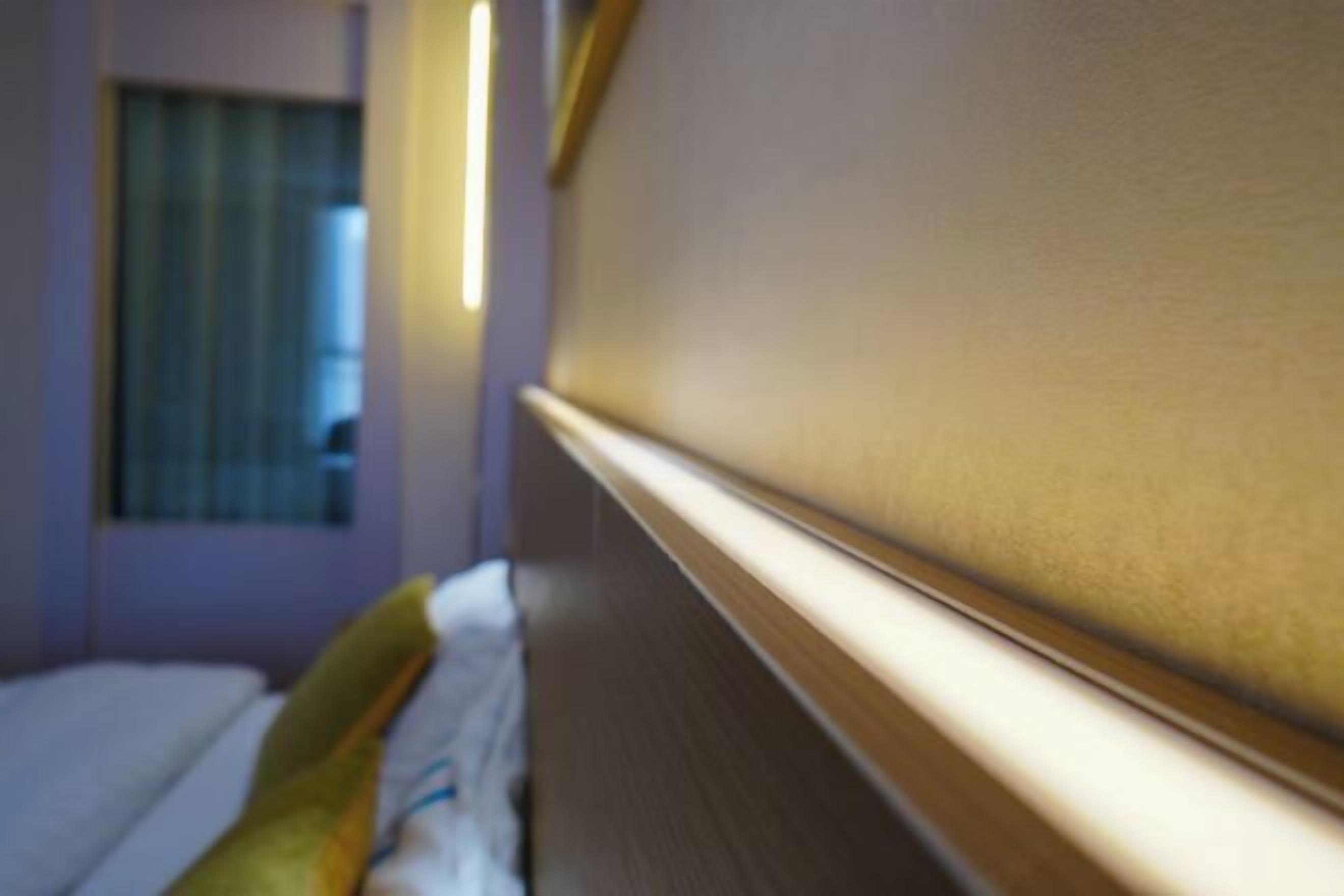 A hotel room with a bed, a window with blinds, and a wall with a light switch.
