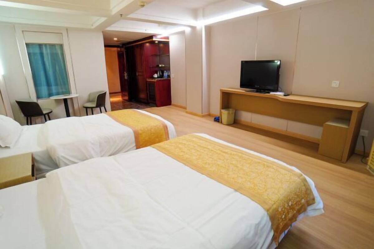 A hotel room with two beds, a desk, a television, and a small seating area.