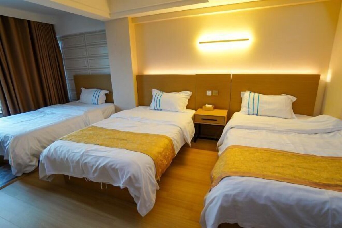 Una habitación de hotel con tres camas individuales, suelo de madera y un diseño moderno para la cabecera.